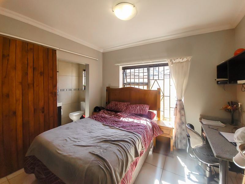 A functional bedroom featuring tiled flooring, a built-in wardrobe with a sliding door, and direct access to an en-suite bathroom.