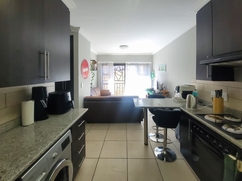 Open-plan kitchen and living area featuring dark cabinetry, granite countertops, built-in appliances, and tiled flooring, leading to a balcony area.