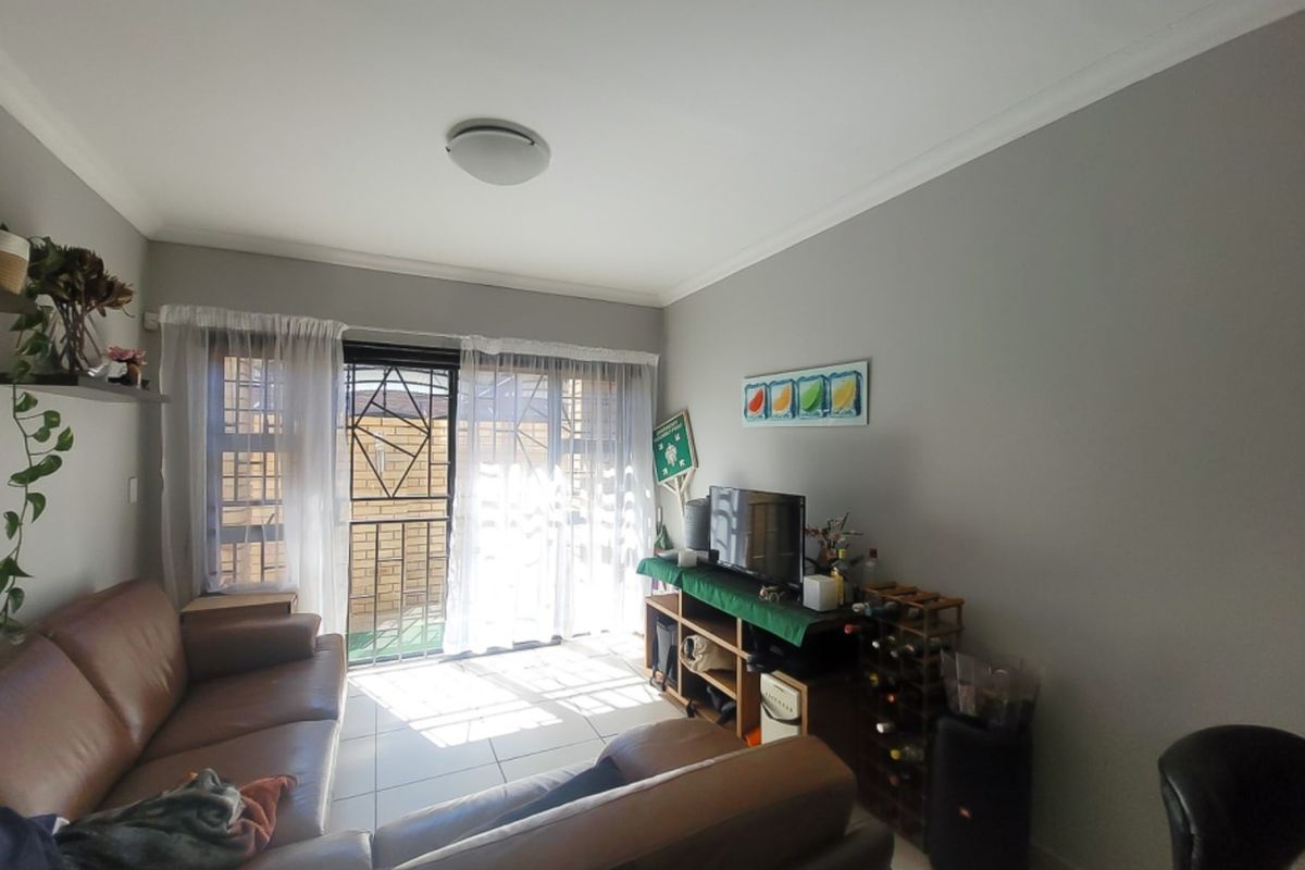 A living room featuring tiled flooring, coved ceilings, and a sliding glass door with a security gate leading to an outdoor area.