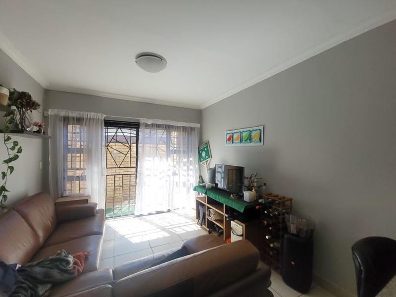 A living room featuring tiled flooring, coved ceilings, and a sliding glass door with a security gate leading to an outdoor area.