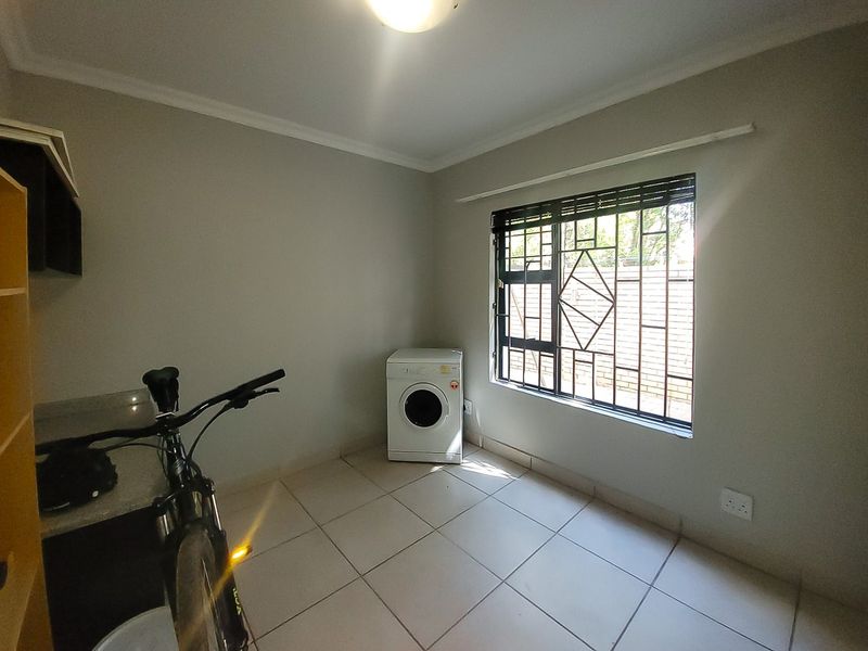 A functional laundry room featuring tiled flooring, built-in cabinetry with a granite countertop, and a window fitted with security bars.