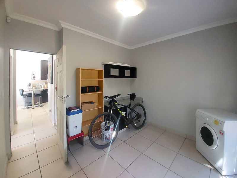 A functional laundry room featuring tiled flooring, built-in shelving, and direct access to the kitchen area.