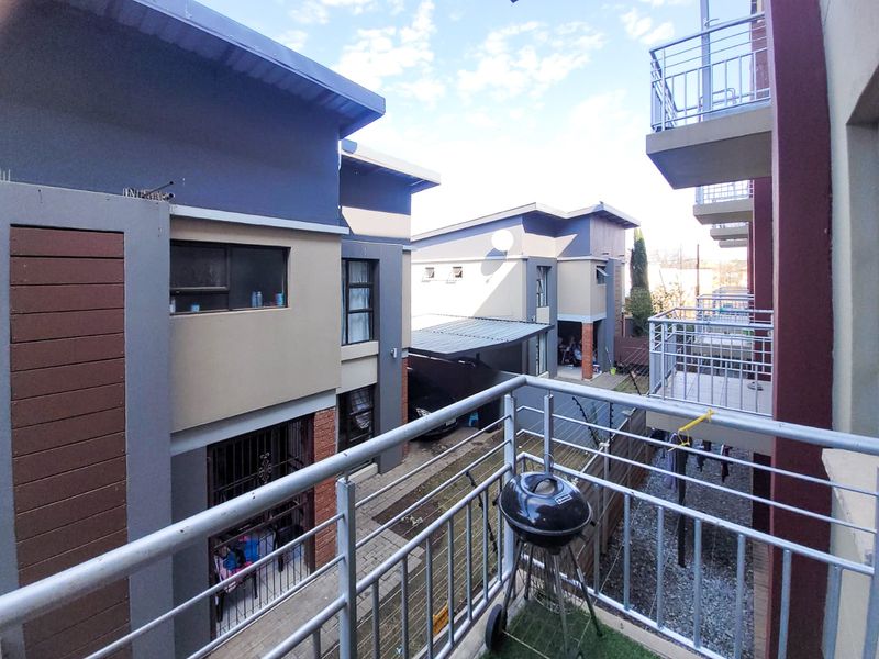 A view from a balcony overlooking the apartment complex courtyard, featuring metal railings and paved ground areas between the residential buildings.