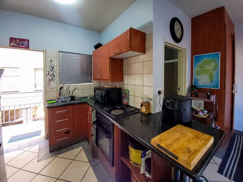 Compact kitchen featuring dark granite countertops, built-in wooden cabinetry, an electric hob, and an integrated oven with direct access to an outdoor balcony area.