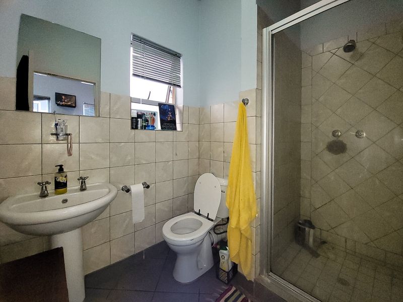 A functional bathroom featuring a pedestal basin, a glass-enclosed shower, and tiled finishes throughout, providing a practical layout for daily use.