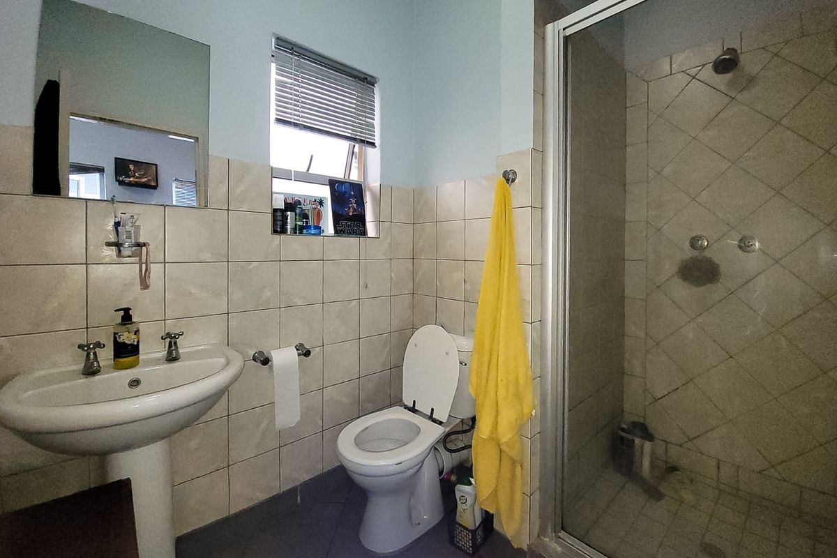 A functional bathroom featuring a pedestal basin, a glass-enclosed shower, and tiled finishes throughout, providing a practical layout for daily use.