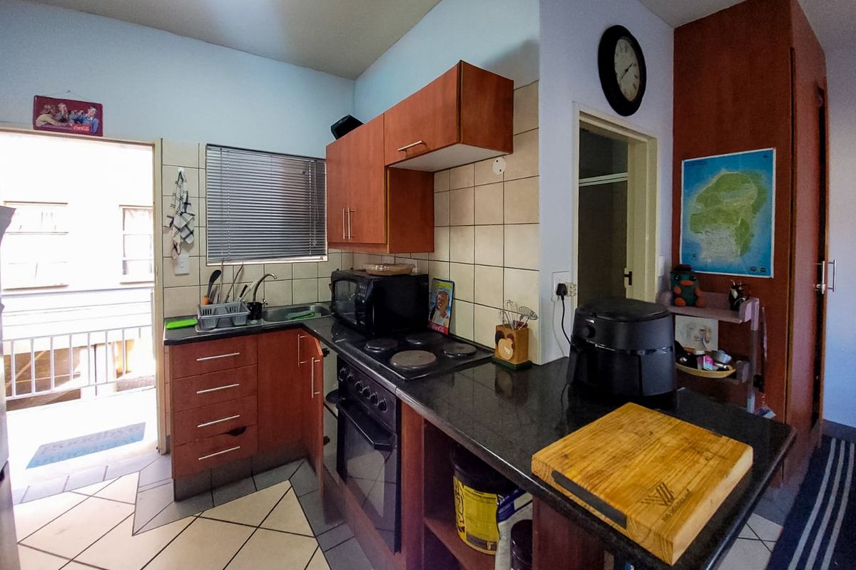 Compact kitchen featuring dark granite countertops, built-in wooden cabinetry, an electric hob, and an integrated oven with direct access to an outdoor balcony area.