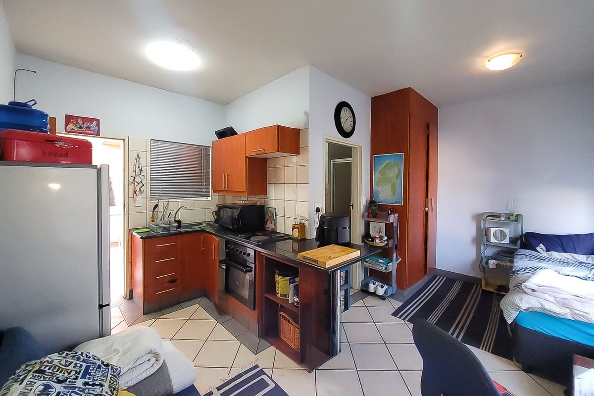 Open-plan studio apartment featuring a compact kitchen with built-in cabinetry, oven, and hob, adjacent to a living and sleeping area with tiled flooring.