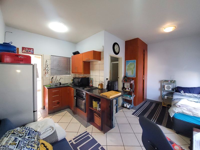 Open-plan studio apartment featuring a compact kitchen with built-in cabinetry, oven, and hob, adjacent to a living and sleeping area with tiled flooring.