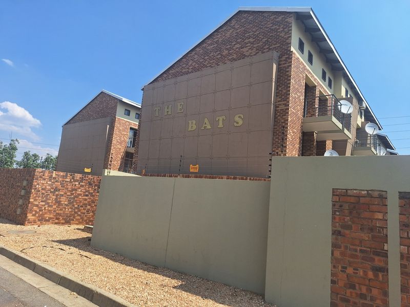 Exterior view of The Bats apartment complex featuring brick and panel facade, perimeter wall with electric fencing, and private balconies.