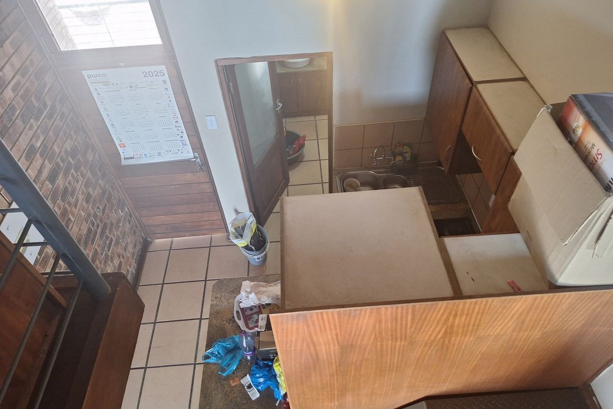 A high-angle view of a dated kitchen featuring tiled flooring, built-in wooden cabinetry, a double bowl sink, and an exposed brick wall.