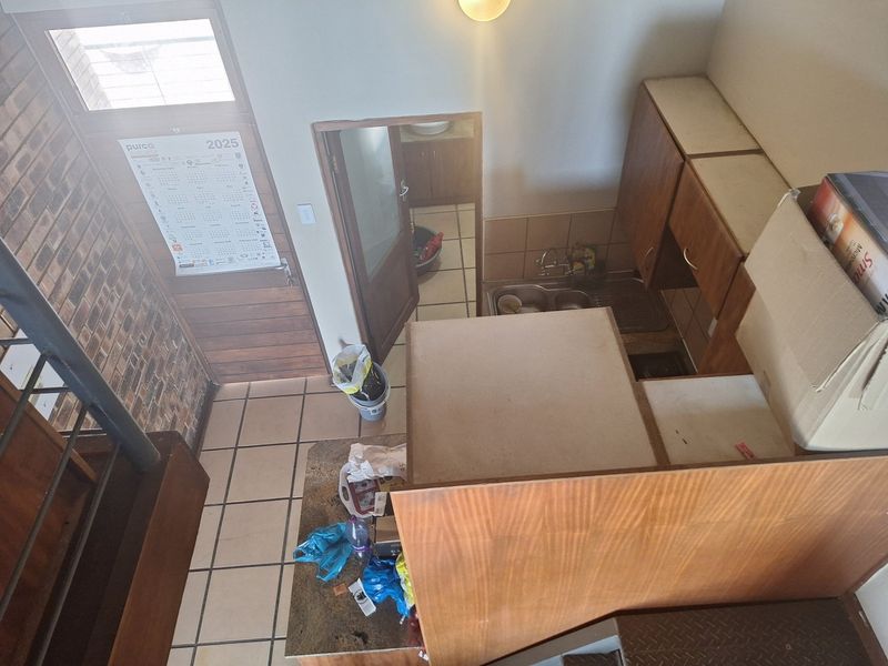 A high-angle view of a dated kitchen featuring tiled flooring, built-in wooden cabinetry, a double bowl sink, and an exposed brick wall.