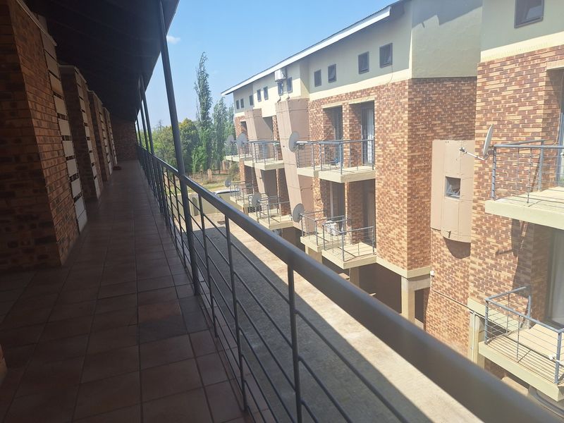 A view from a covered apartment balcony overlooking the building exterior, featuring brick facade details and metal safety railings.