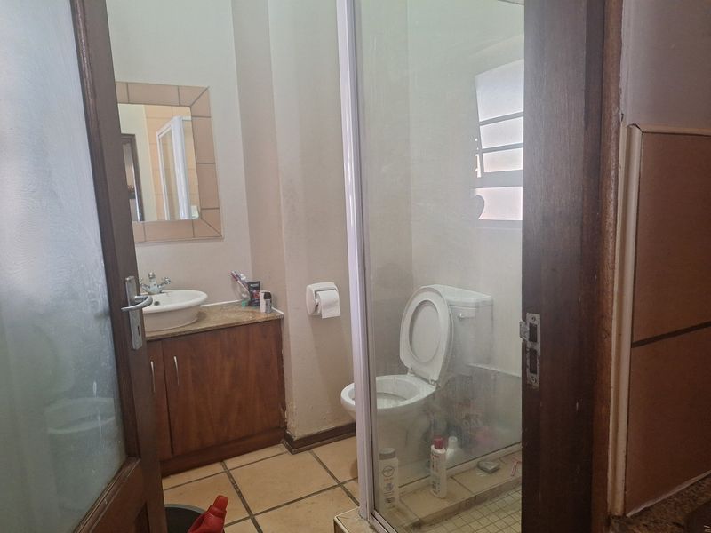 A functional bathroom featuring a vanity cabinet with basin, a glass-enclosed shower, and tiled flooring, offering a practical layout with potential for cosmetic updates.