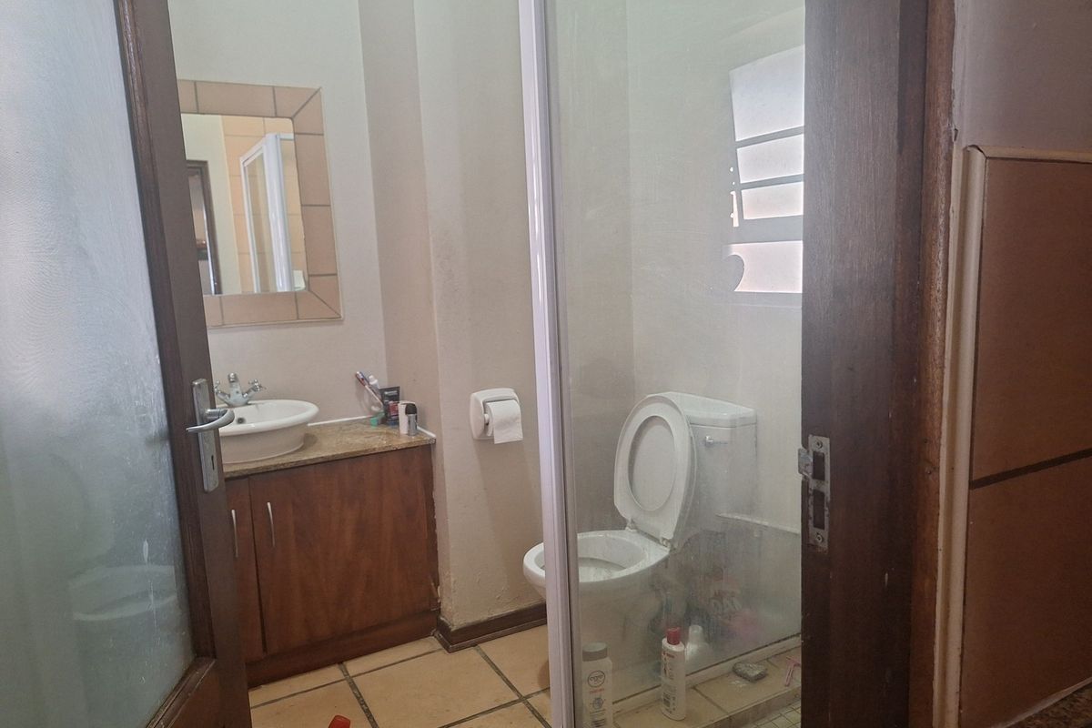 A functional bathroom featuring a vanity cabinet with basin, a glass-enclosed shower, and tiled flooring, offering a practical layout with potential for cosmetic updates.