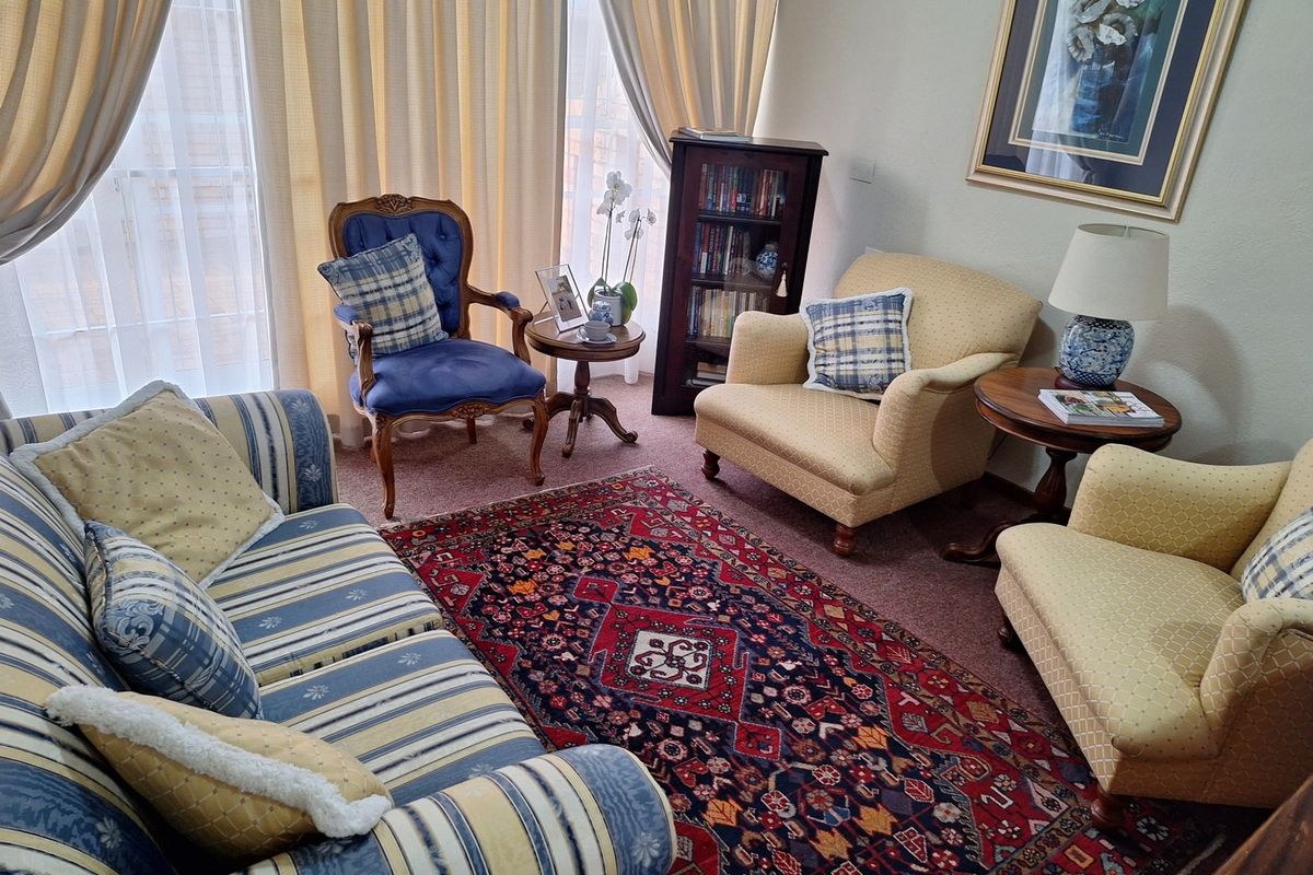 A comfortable living room featuring carpeted flooring and large windows with floor-to-ceiling curtains, providing ample natural light.