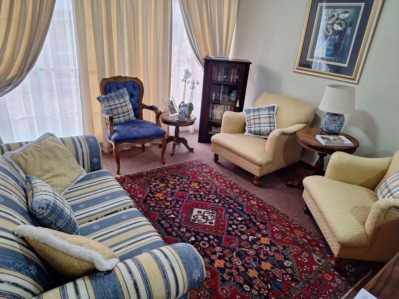 A comfortable living room featuring carpeted flooring and large windows with floor-to-ceiling curtains, providing ample natural light.