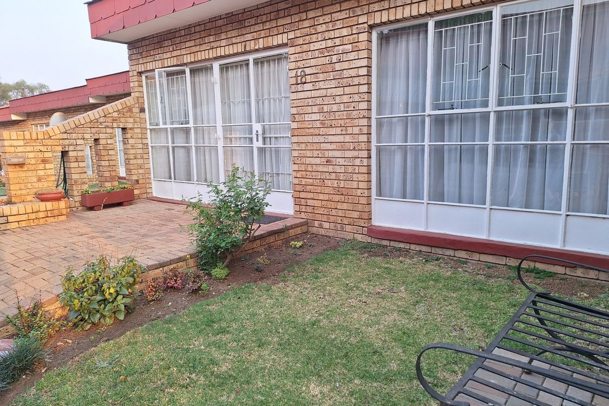 Rear exterior view of an apartment featuring a face brick facade, paved patio area, and a small private lawn.
