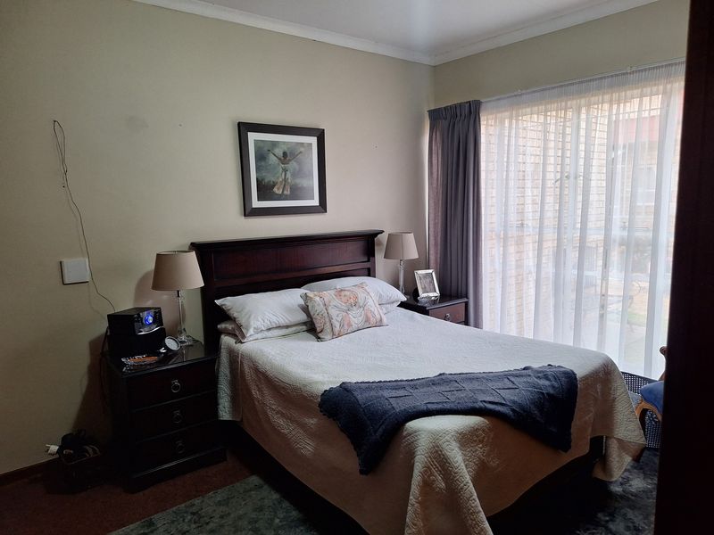 A standard bedroom featuring neutral walls, coving, and large windows with curtain rails, providing natural light.