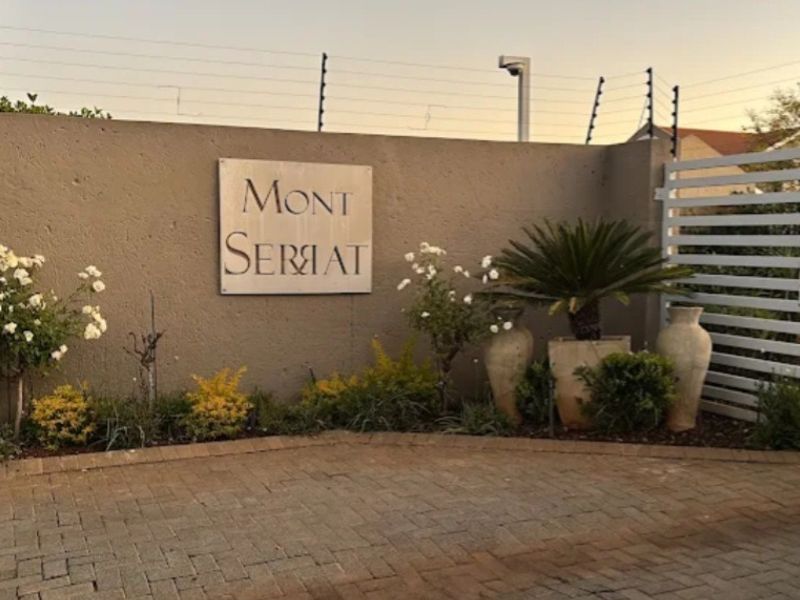 The entrance to Mont Serrat complex featuring a secure boundary wall, electric fencing, and a gated access point with paved driveway.