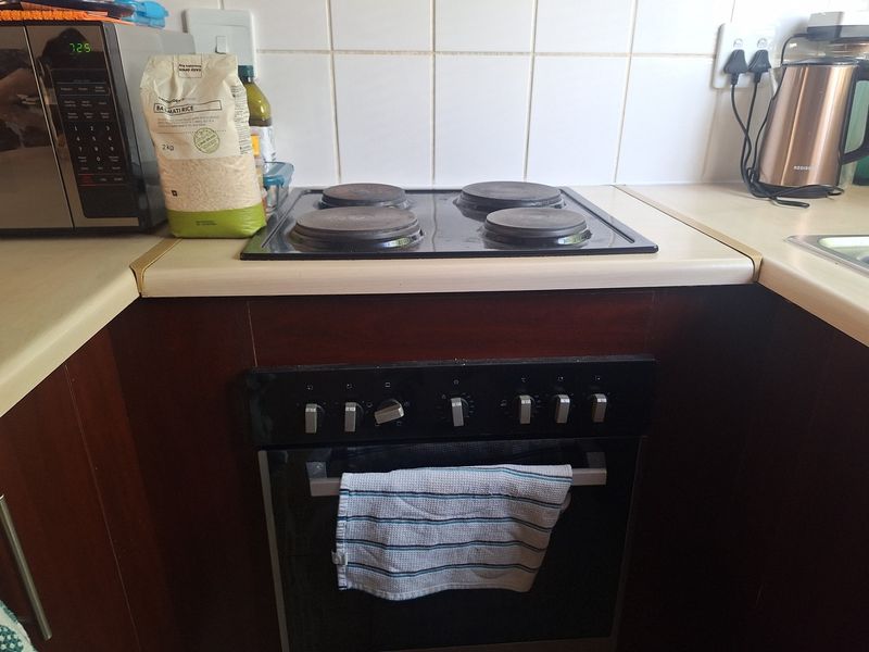 A functional kitchen area featuring a built-in oven, electric hob, and tiled backsplash with laminate countertops.