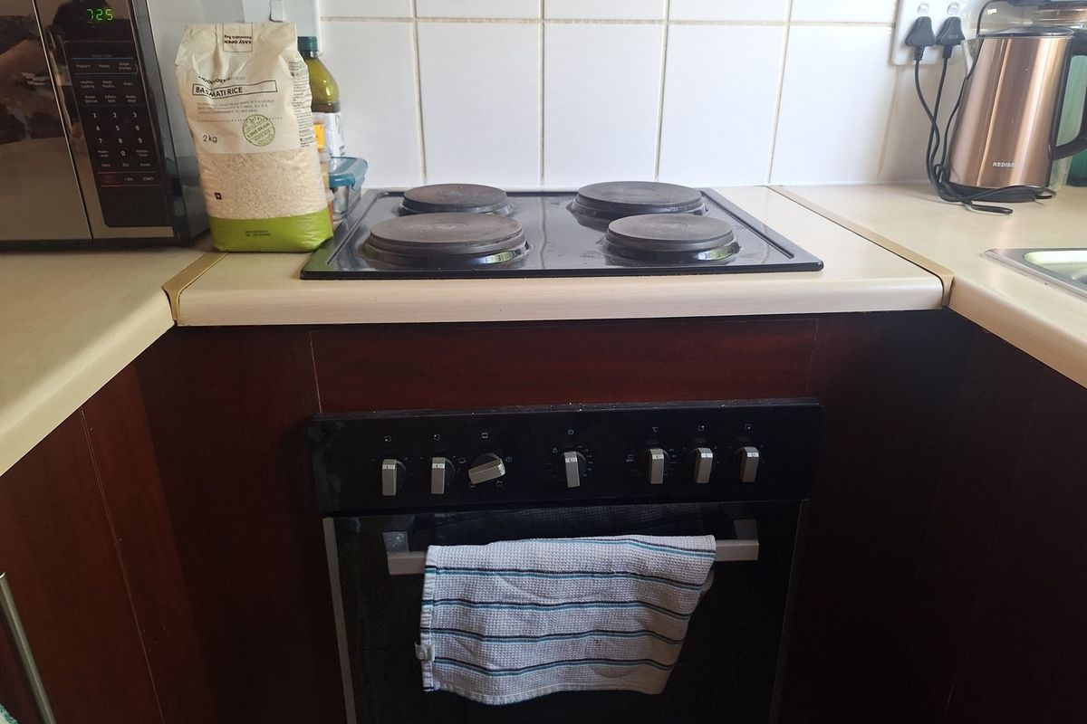 A functional kitchen area featuring a built-in oven, electric hob, and tiled backsplash with laminate countertops.
