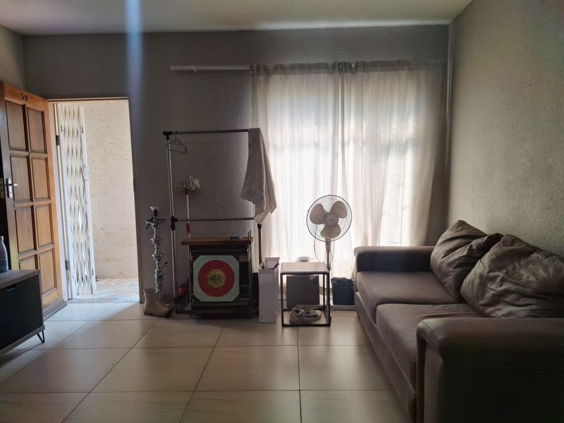 A living room area featuring tiled flooring, a timber entrance door, and a security gate leading to an outdoor space.
