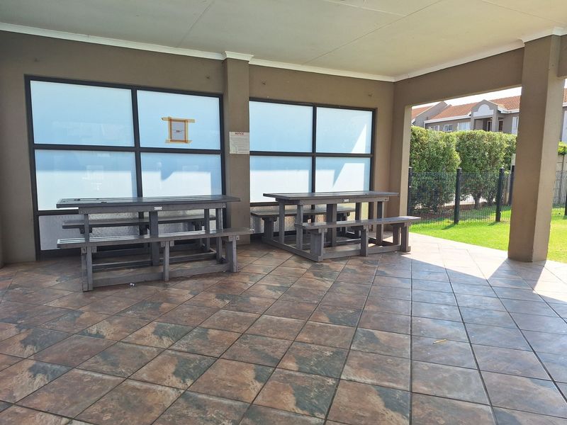 A covered outdoor patio area featuring tiled flooring and large aluminum-framed windows, providing a functional space for communal or outdoor use.