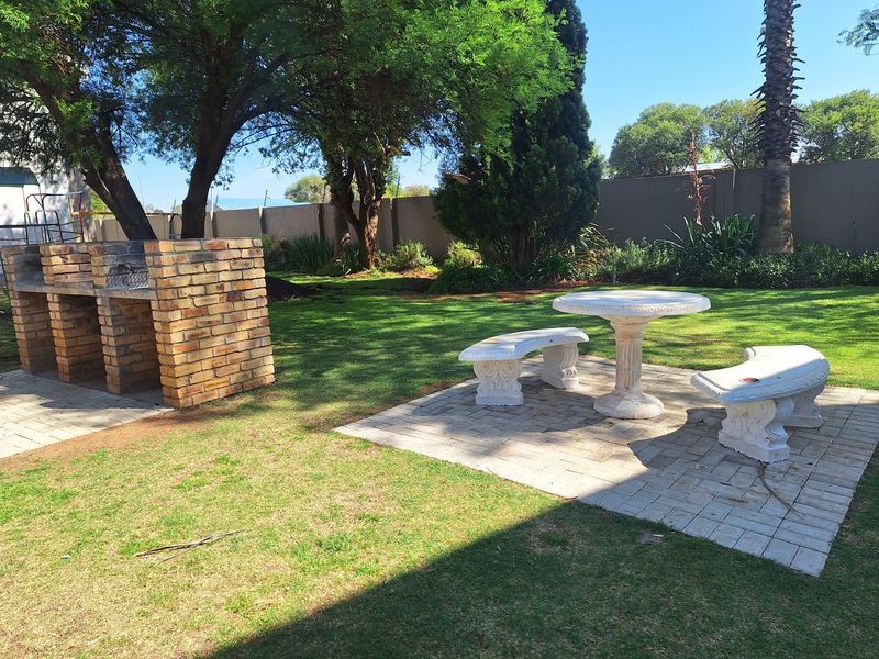 A well-maintained garden featuring a built-in brick braai and a paved seating area, enclosed by a perimeter wall.