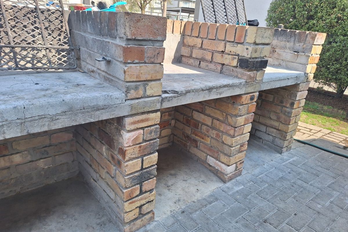 Outdoor entertainment area featuring a large built-in brick braai with concrete countertops and paved patio flooring.