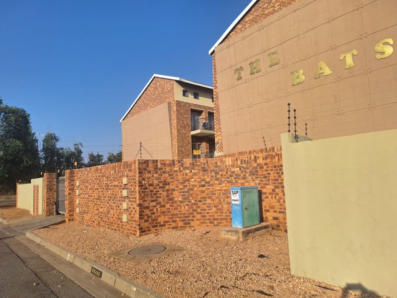 Exterior view of the apartment complex entrance featuring face brick boundary walls, secure electric fencing, and paved access.