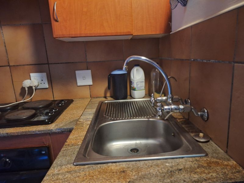 A functional kitchen area featuring a stainless steel sink, granite countertops, an electric hob, and built-in cabinetry with a tiled backsplash.
