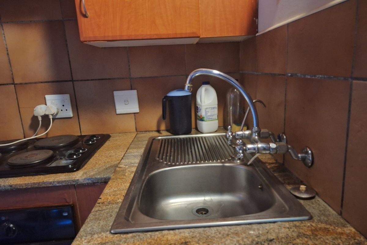 A functional kitchen area featuring a stainless steel sink, granite countertops, an electric hob, and built-in cabinetry with a tiled backsplash.