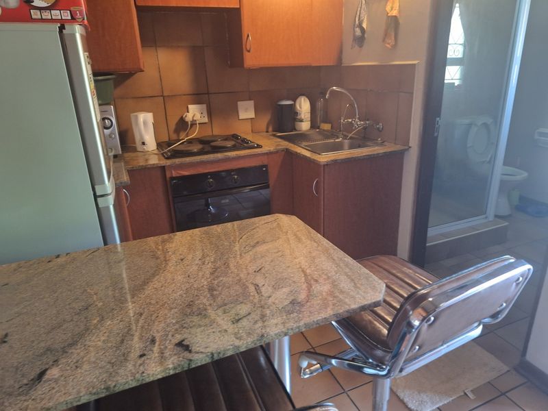 Compact kitchen featuring granite countertops, built-in oven, electric hob, and tiled backsplash with adjacent access to the bathroom area.