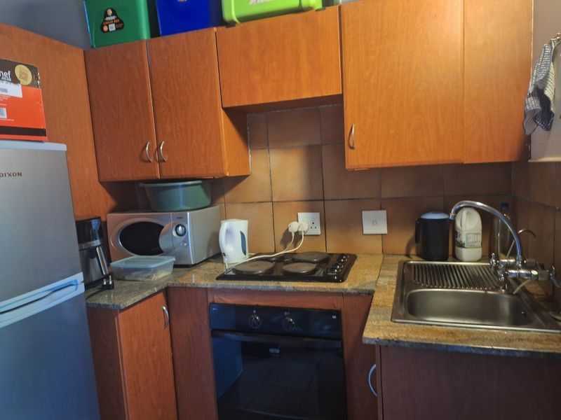 Compact kitchen featuring wooden cabinetry, granite countertops, a built-in oven, electric hob, and a stainless steel sink with tiled backsplash.