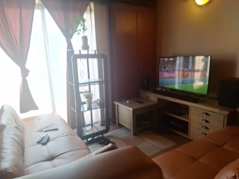 A living room area featuring tiled flooring and a built-in storage cupboard, with access to a balcony through a glass sliding door.