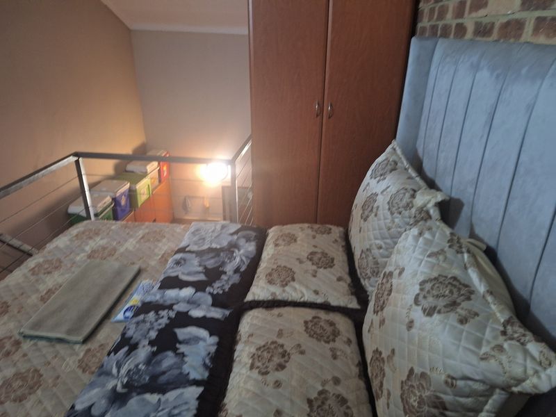 A loft-style bedroom featuring an exposed brick wall, built-in wardrobe, and a metal balustrade overlooking the lower level.