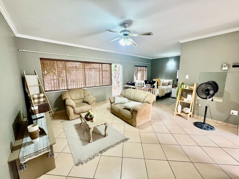 An open-plan living area featuring tiled flooring, a ceiling fan, and direct access to an outdoor space through a security gate.