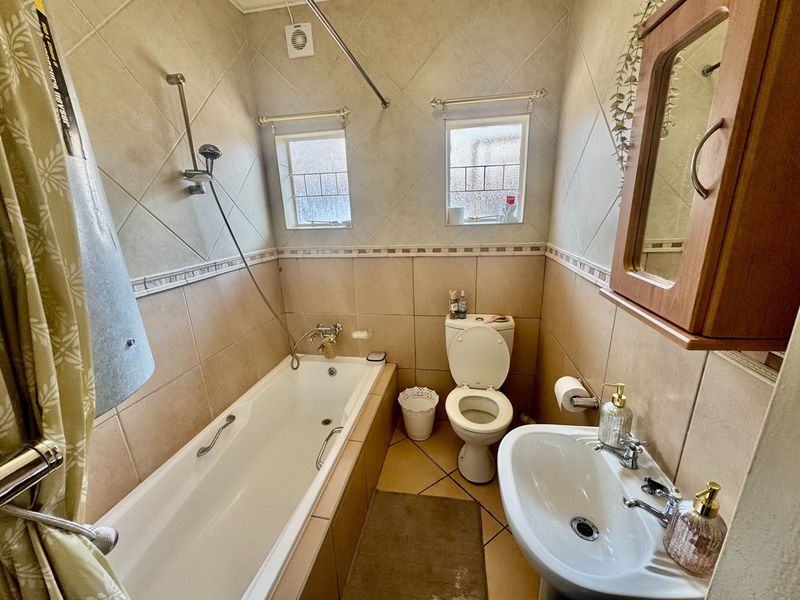A functional bathroom featuring a bathtub with shower mixer, pedestal basin, and toilet, finished with neutral wall and floor tiling.