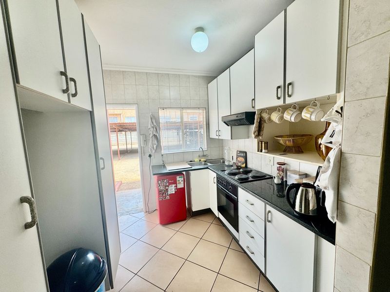 A functional kitchen featuring white cabinetry, granite countertops, built-in oven and hob, tiled backsplash, and direct access to the exterior.