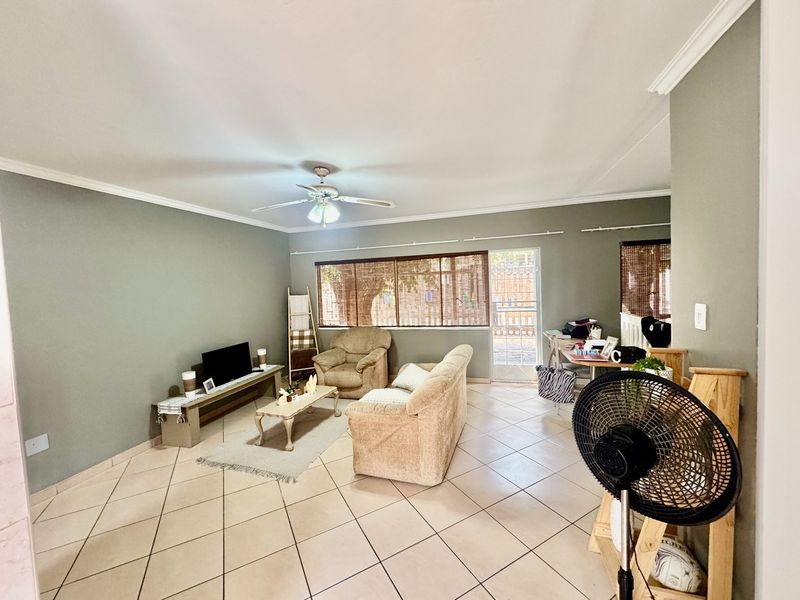 A spacious living room featuring neutral wall tones, ceramic tiled flooring, crown molding, and a ceiling fan, with direct access to an outdoor area.