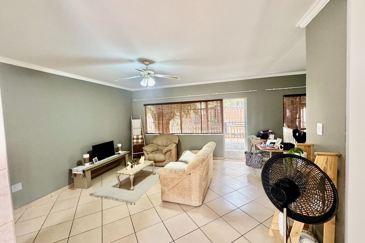 A spacious living room featuring neutral wall tones, ceramic tiled flooring, crown molding, and a ceiling fan, with direct access to an outdoor area.