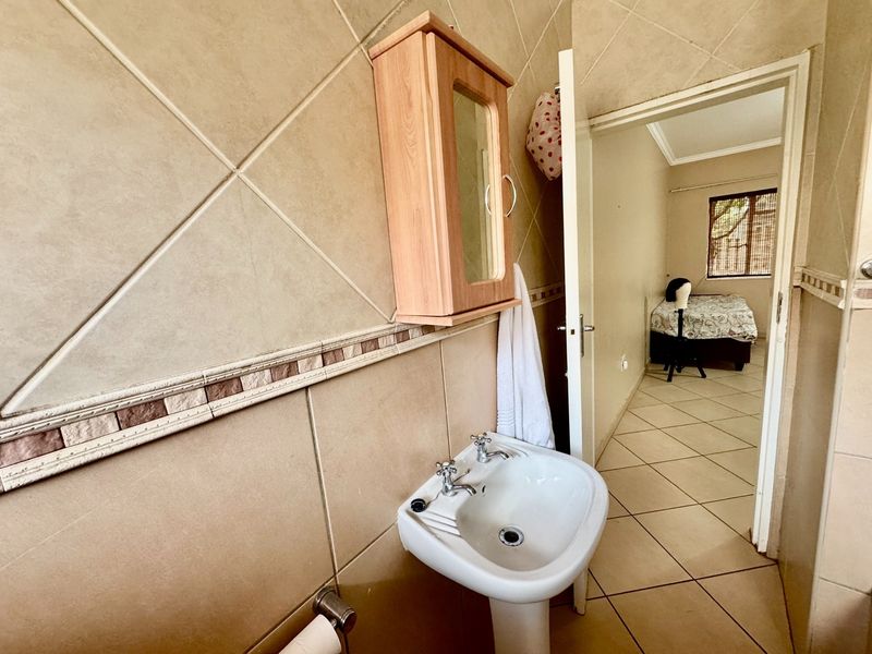 A functional bathroom featuring a pedestal basin, wall-mounted medicine cabinet, and neutral ceramic tiling, with a view into the adjacent bedroom.