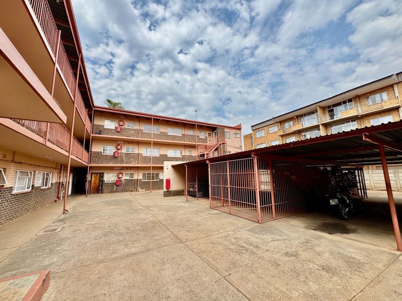 Exterior view of an apartment complex courtyard featuring brick facade buildings, covered parking bays, and communal balcony walkways.
