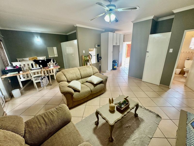 Spacious living area featuring tiled flooring, ceiling fan, and built-in storage cupboards, with direct access to an adjacent bathroom.