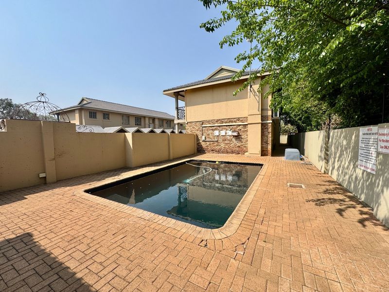 Outdoor swimming pool area featuring brick paving and high boundary walls, providing a private communal space for residents.