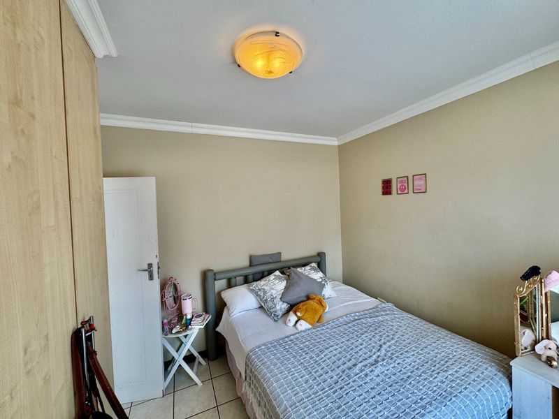 A functional bedroom featuring tiled flooring, a built-in wardrobe, and decorative ceiling cornicing, providing a neutral base for personalization.