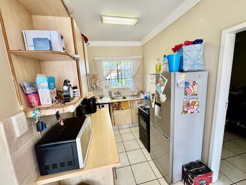 A compact kitchen featuring laminate countertops, built-in cabinetry, a stainless steel sink, and ceramic tile flooring, offering a functional layout with potential for modernization.