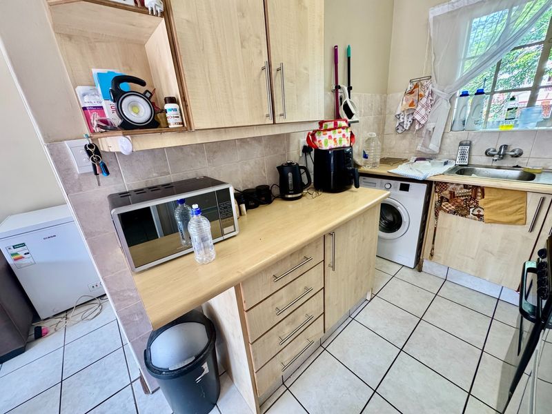 Functional kitchen area featuring light wood-finish cabinetry, tiled backsplash, ceramic flooring, and integrated space for a washing machine.
