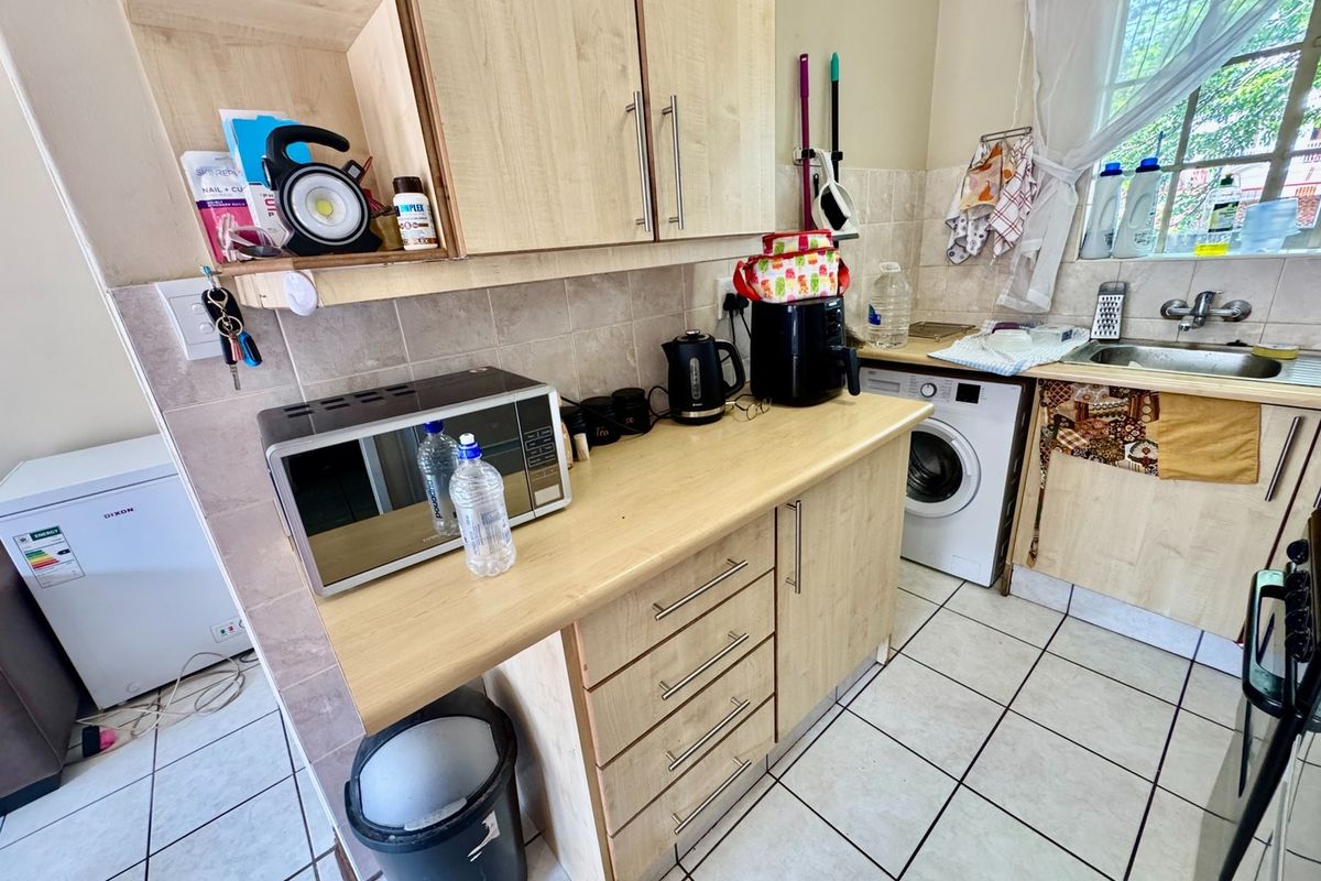Functional kitchen area featuring light wood-finish cabinetry, tiled backsplash, ceramic flooring, and integrated space for a washing machine.